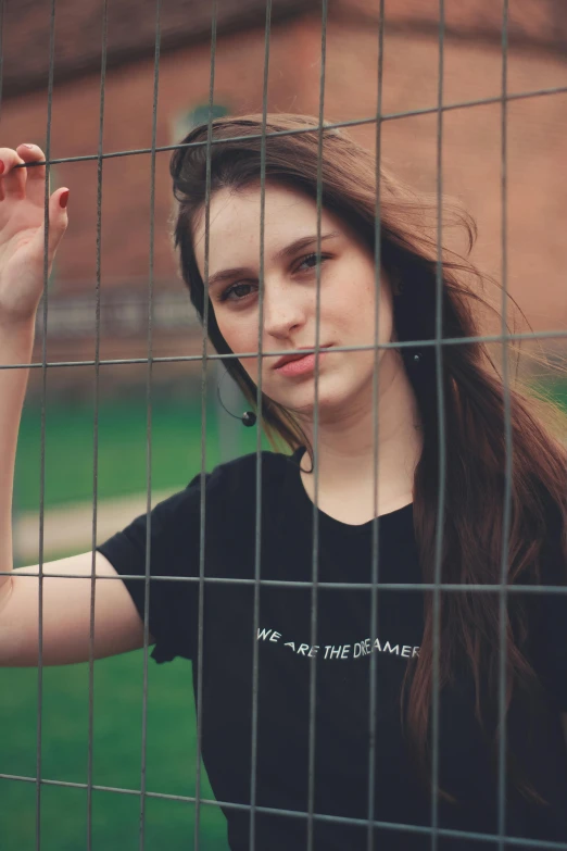 a young woman poses behind a wire fence