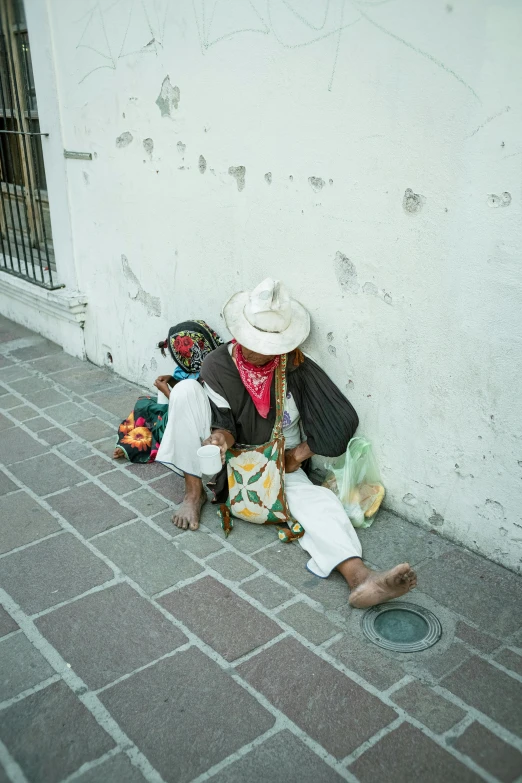 two women sitting and leaning against a wall with hats on