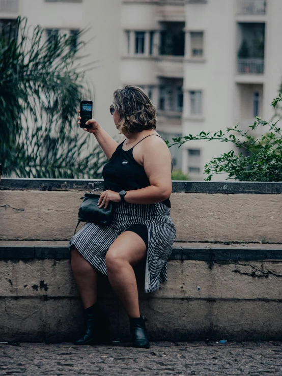 a woman sitting on a wall while taking a picture with her phone