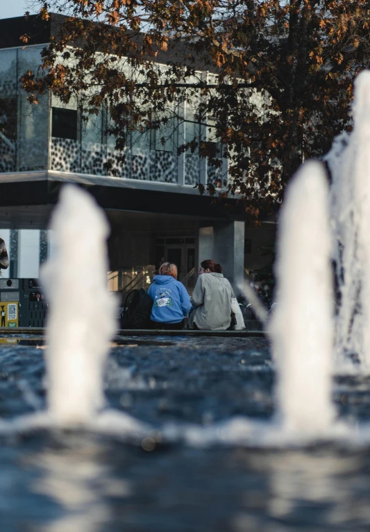 two people sitting next to a fountain on the street