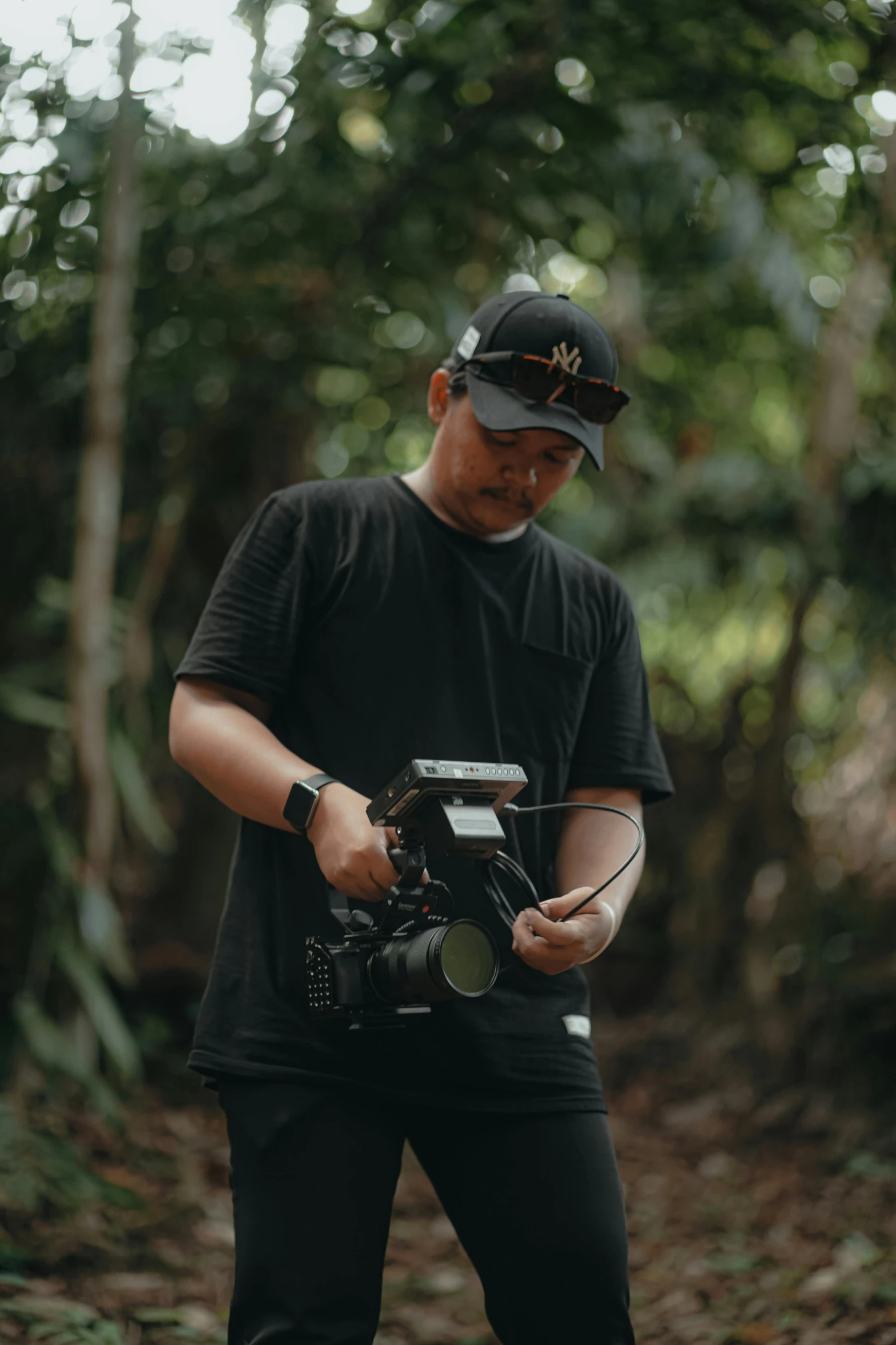 man holding camera near forest and looking down at phone