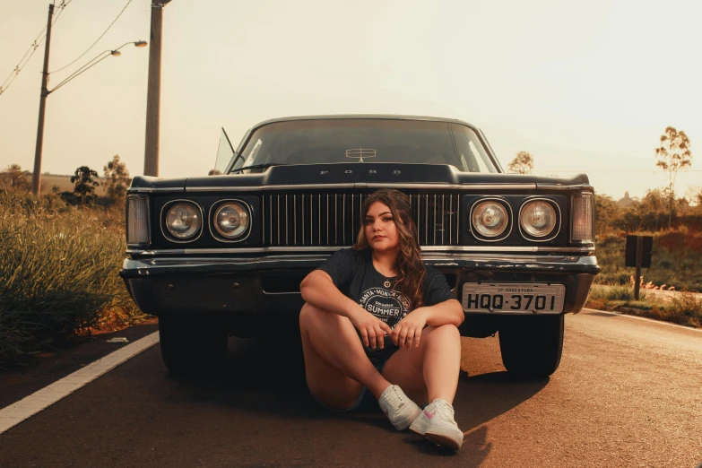 a young woman sitting in front of an old car