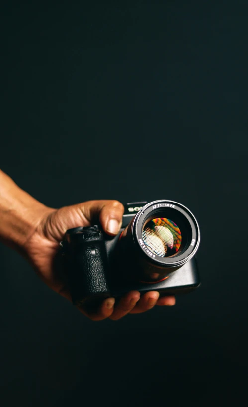 a hand holding a digital camera on a dark background