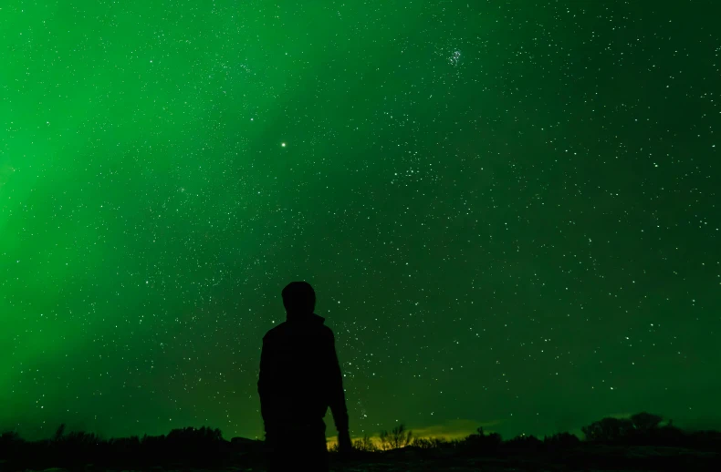 a man stands silhouetted against an almost lit night sky