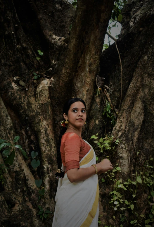 a woman standing next to a tree while holding a piece of paper