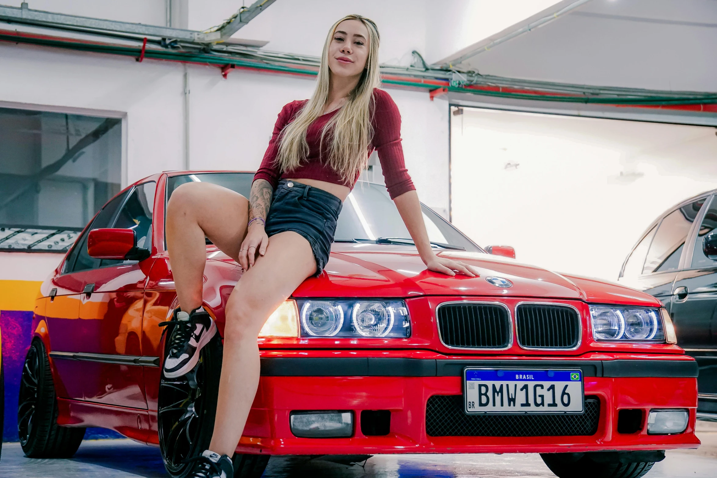 a young woman in tights sitting on the hood of a red car