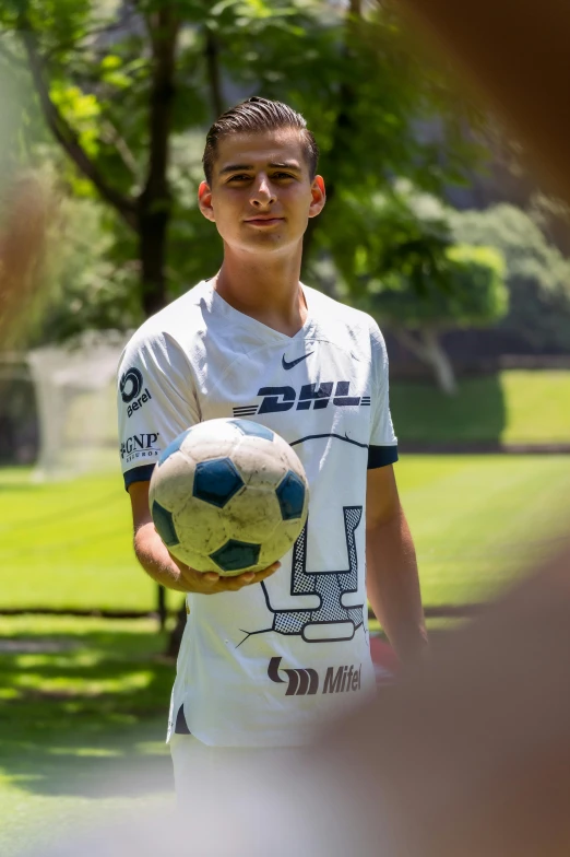 a young man holding a soccer ball with a field in the background