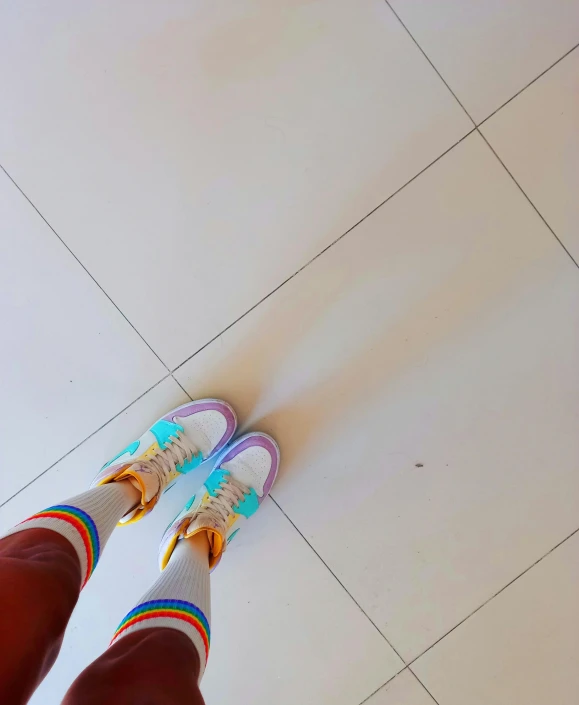 a person is standing on the floor holding onto their white and colorful shoes