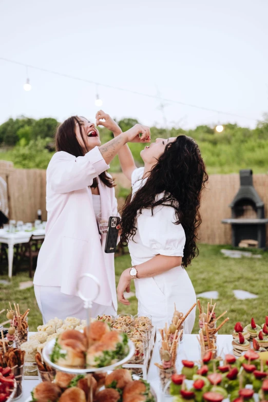 two women are standing at a table with food on it