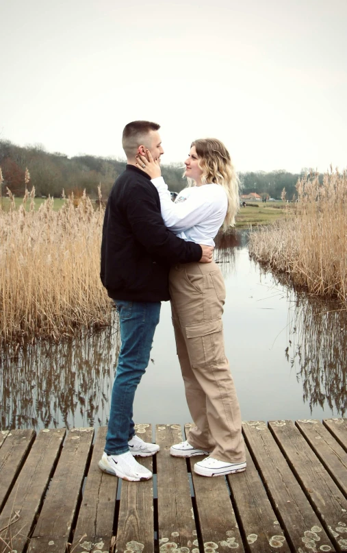 a man and woman emcing on the dock next to a lake