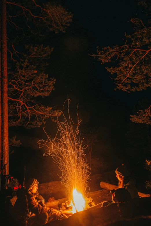 a campfire lit up in the night with friends sitting around it