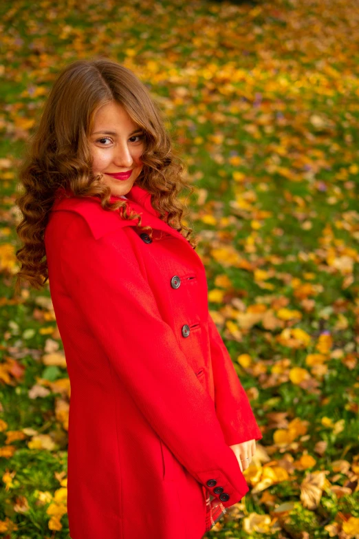 a woman wearing a red coat is standing in leaves