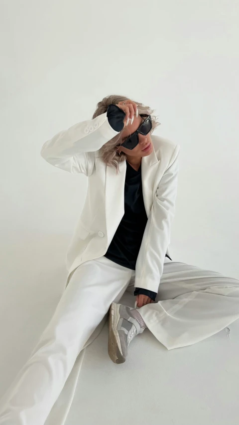 a woman sitting on the ground wearing white suit and black top hat