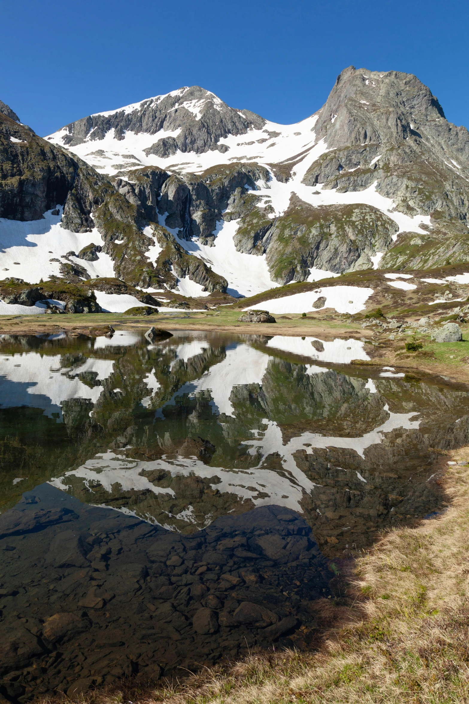 a mountain reflecting in the water on top of a grassy hill