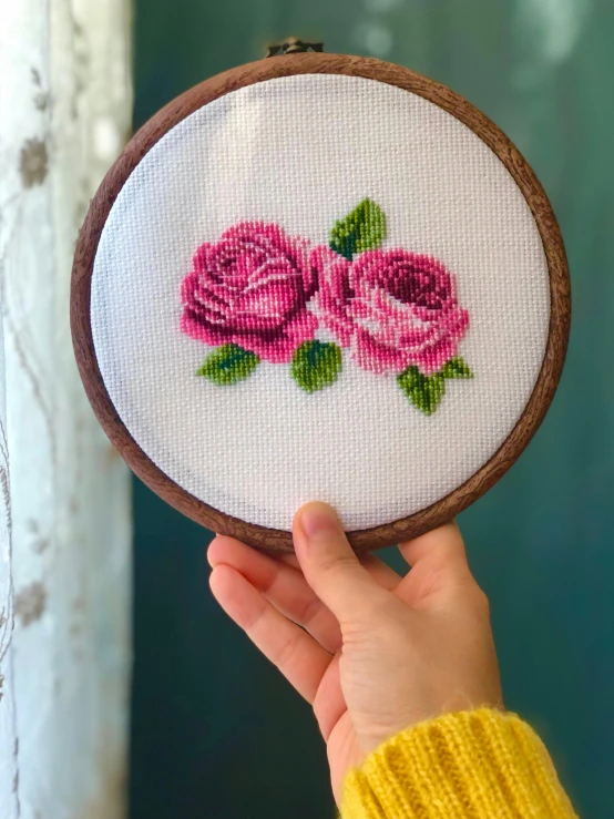 someone is holding a hand embroidered pink rose