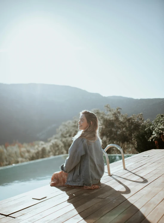 woman in grey top sitting on deck next to large body of water