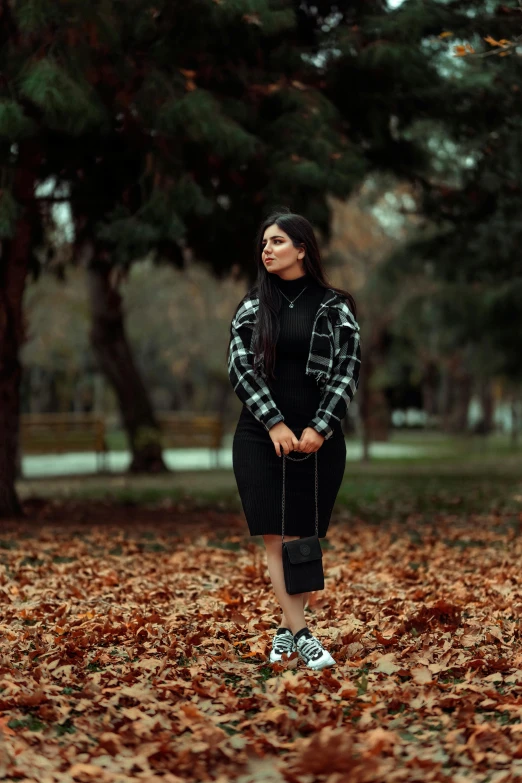 the young woman is standing in a park with fallen leaves