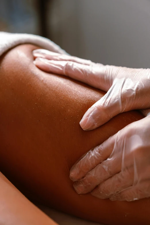 a person in white gloves holds their leg up while touching the  of another person in a tan colored room