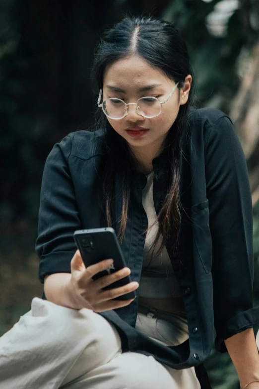 a woman in glasses sitting on the ground and looking at her cell phone