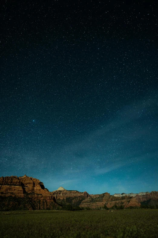 a distant mountain range with grass and trees under the stars