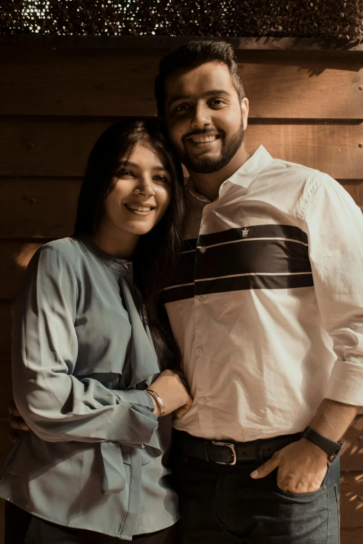 a man and a woman pose together in front of a wood wall