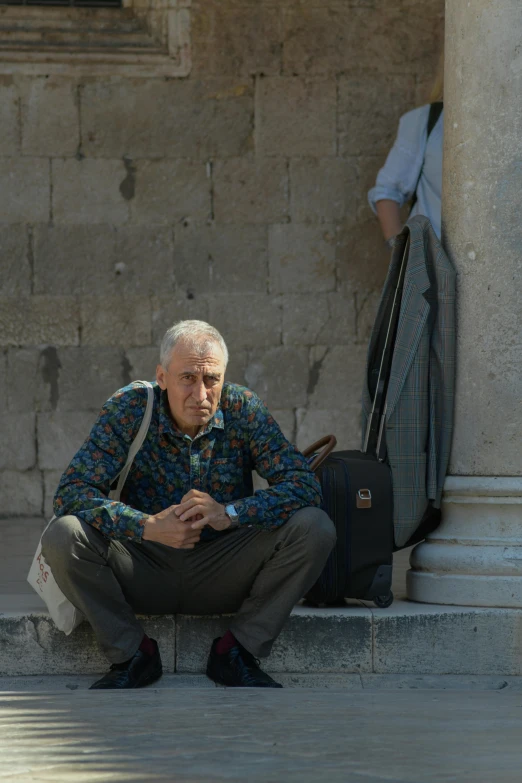 a person sitting outside a building next to a bag of luggage