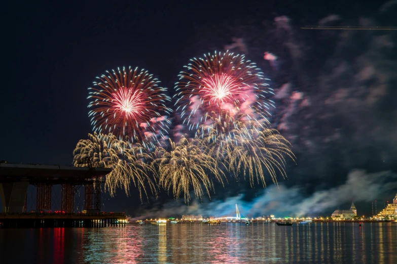 a number of fireworks floating near water with buildings in the background