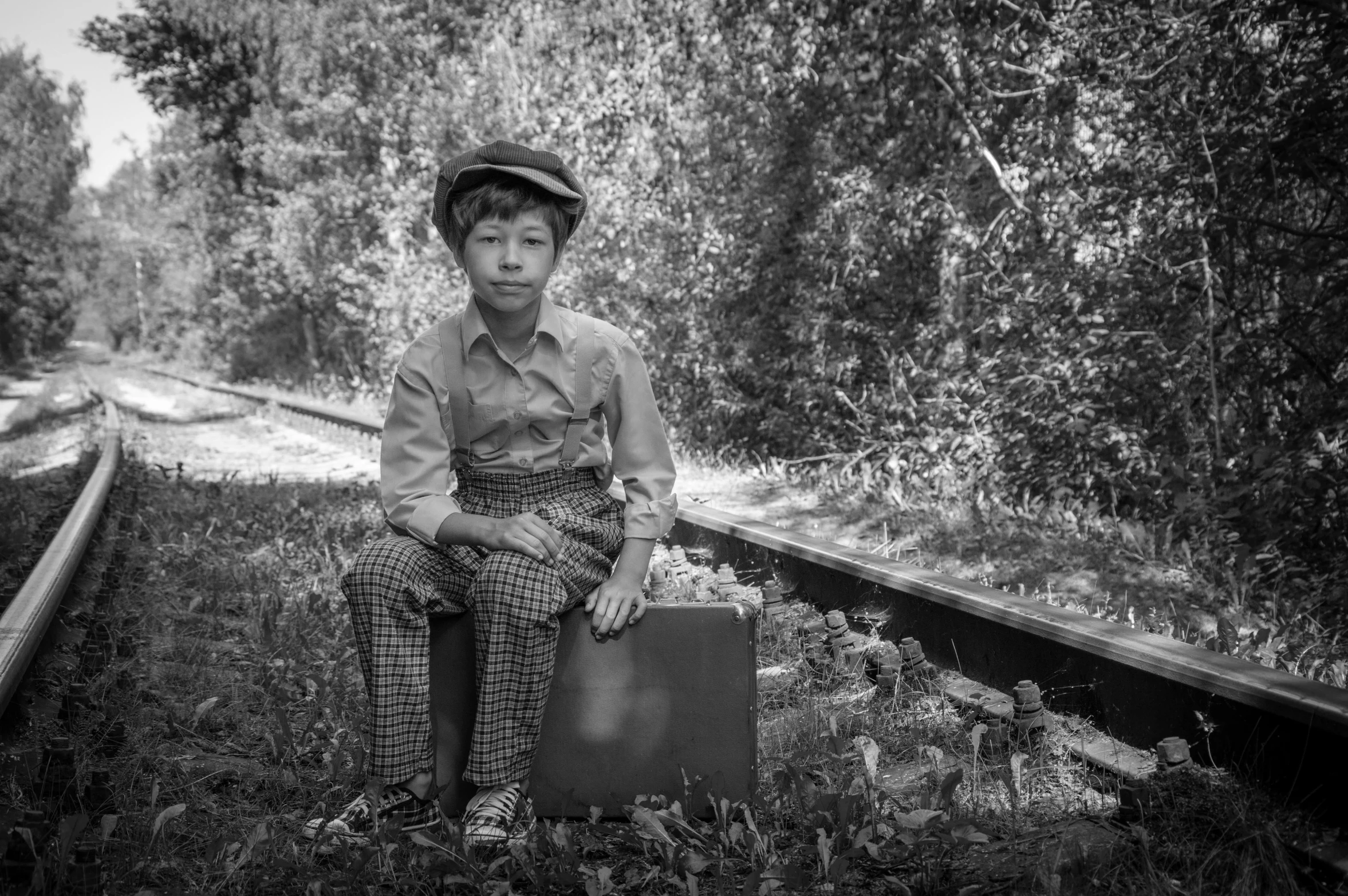 black and white image of a boy sitting on train tracks