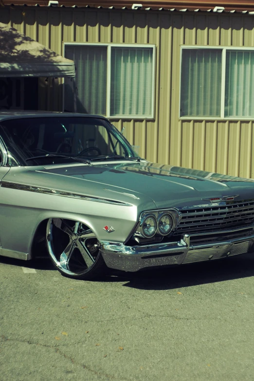 an old gray car parked next to a tan building