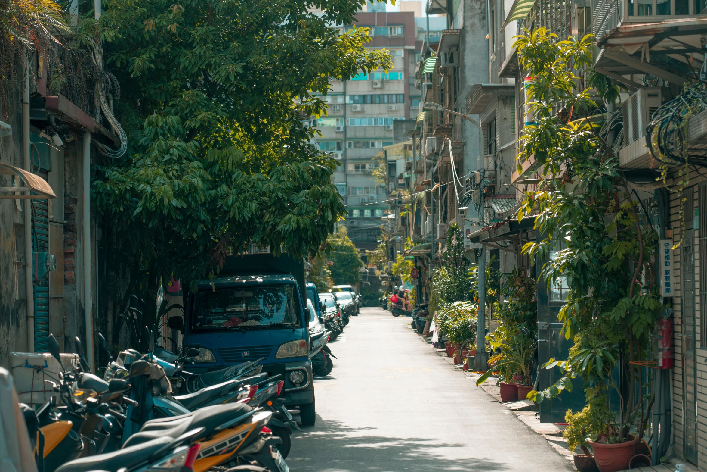 a narrow city street with parked bikes and cars