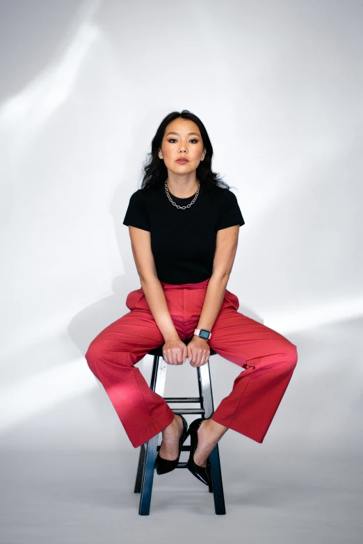 a woman in a black shirt and red pants sitting on a chair