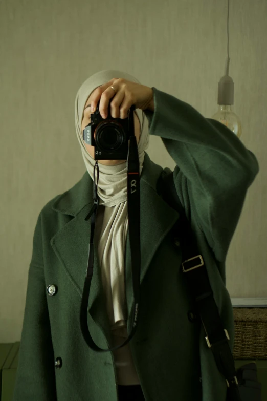 a young woman in a green jacket holding her camera and a white scarf