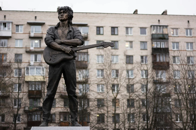 a statue of a man holding an electric guitar in front of a building