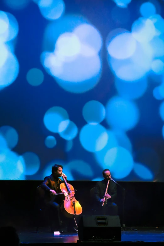 two musicians perform on a stage while large blue lights are projected behind them