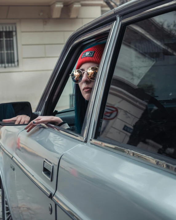 a woman wearing sunglasses and hat leaning out the window of a car