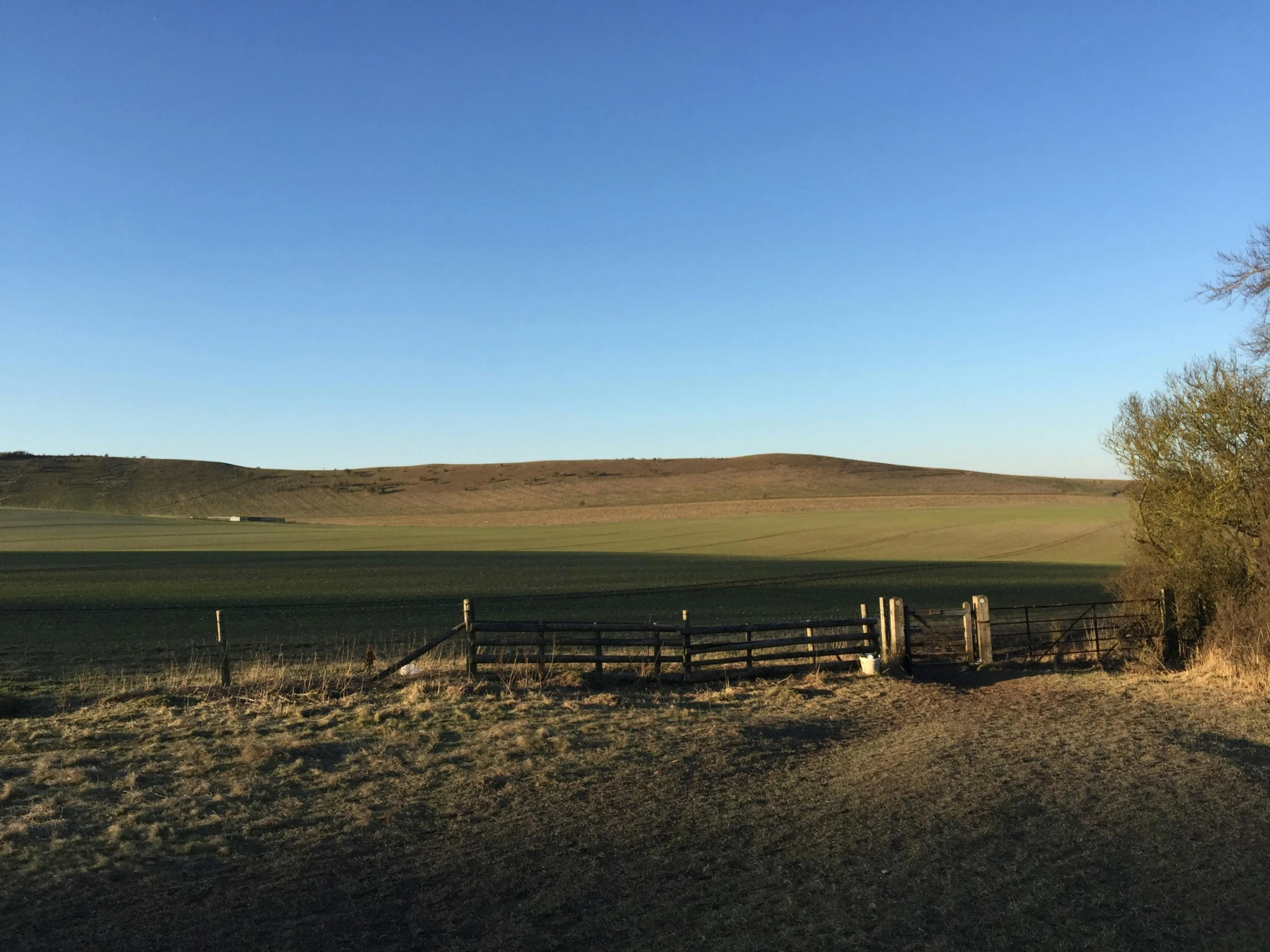 an empty open field with a fence, trees and hills in the background