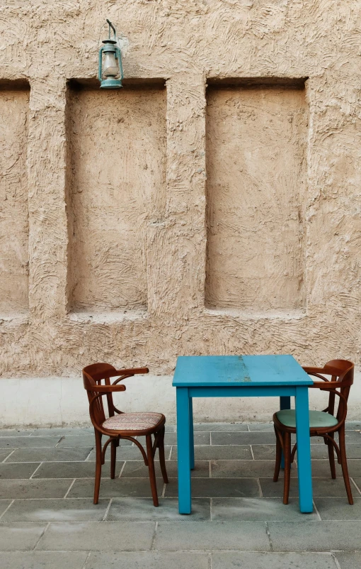 a blue table sitting next to two chairs in front of a brown wall