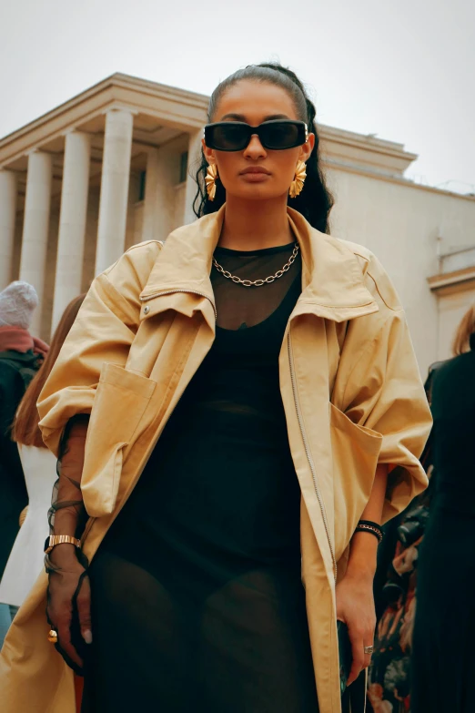 a young black woman wearing an oversized yellow trench jacket and sunglasses