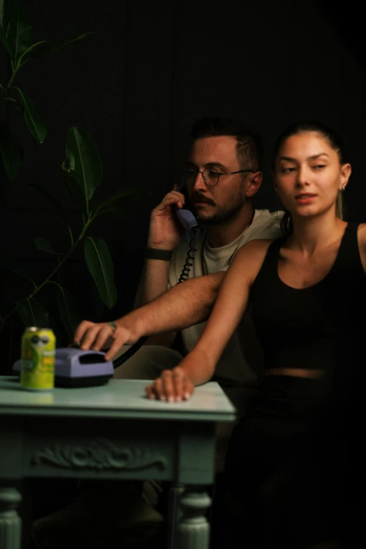 a young woman sitting at a table next to a man with a phone