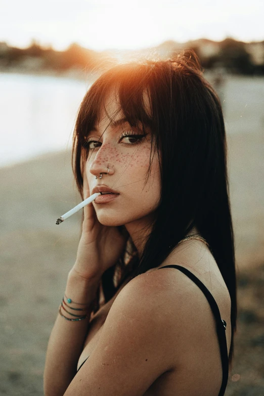 a beautiful young lady sitting on the beach smoking