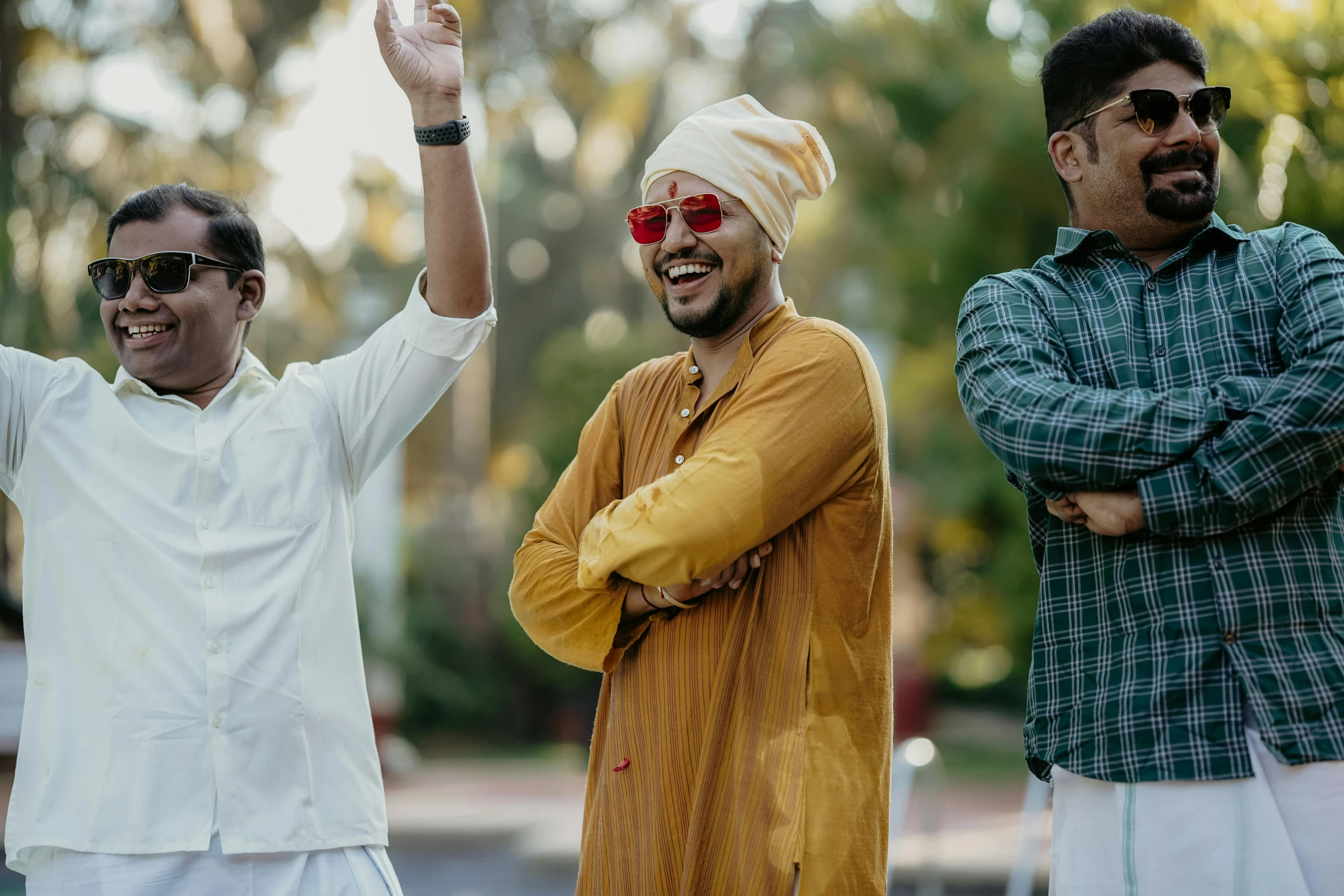 four people wearing white clothes and sunglasses standing with one waving