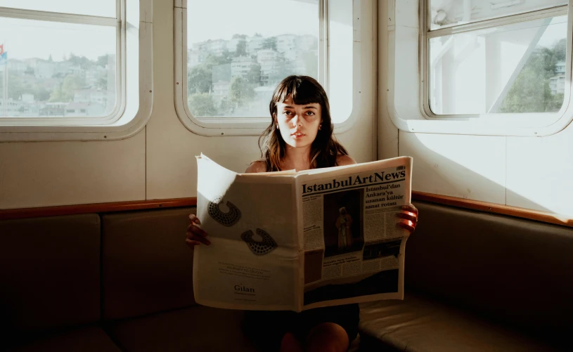 a young woman sitting on a train with a newspaper in her hands