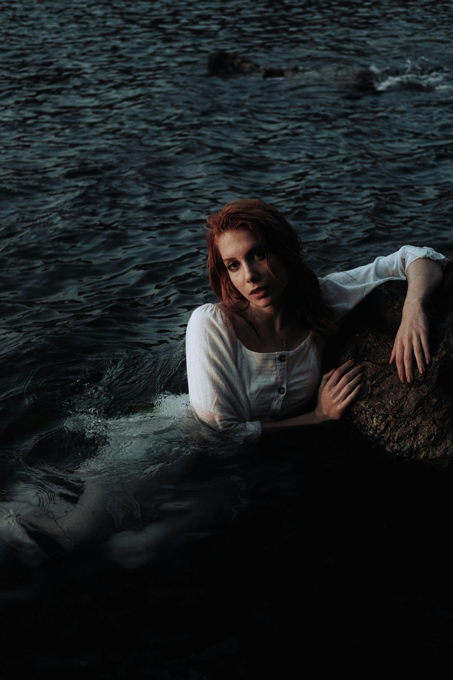 a woman sitting in water holding a rock