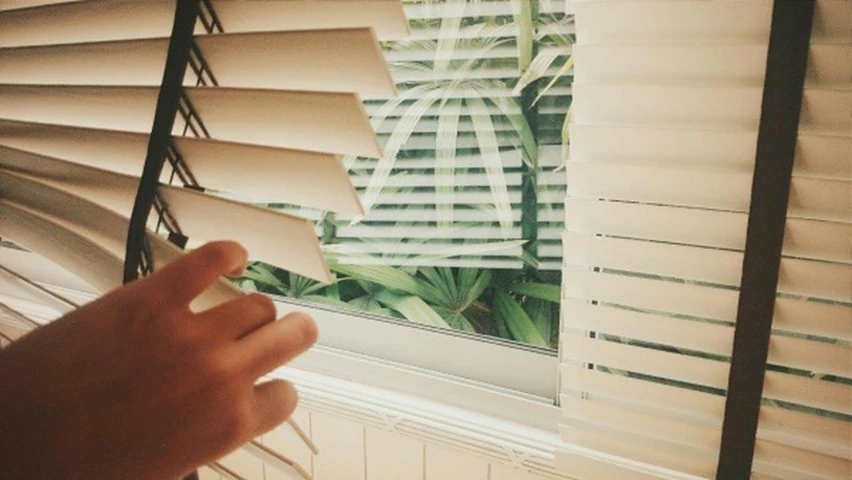 a hand reaching for blinds to look out the window