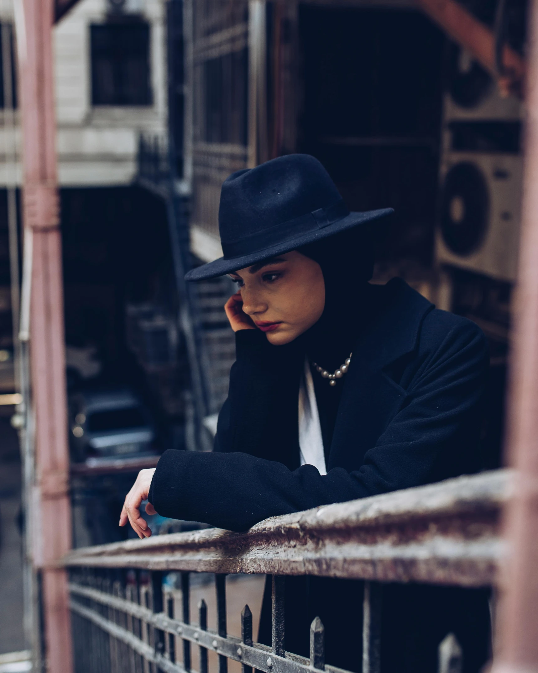 a woman leaning on a metal railing with a fedora