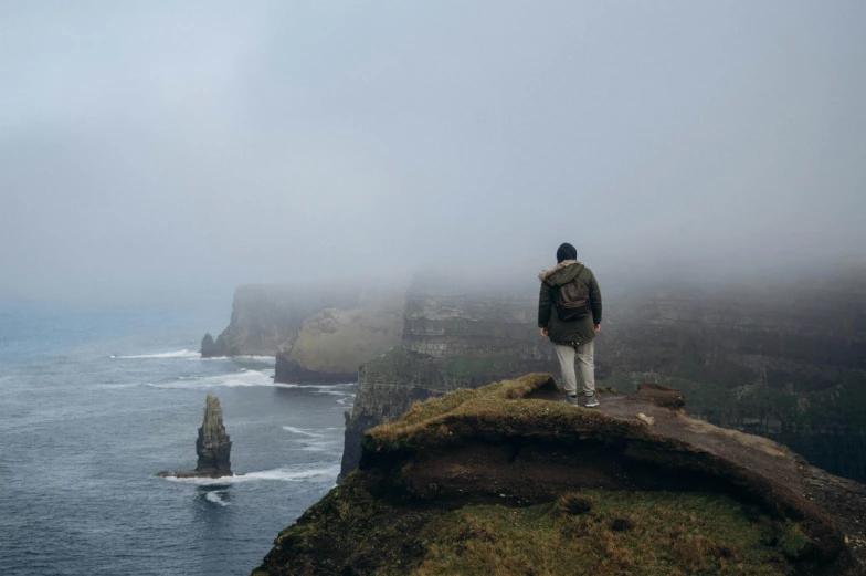 person standing on a cliff with a foggy sky above