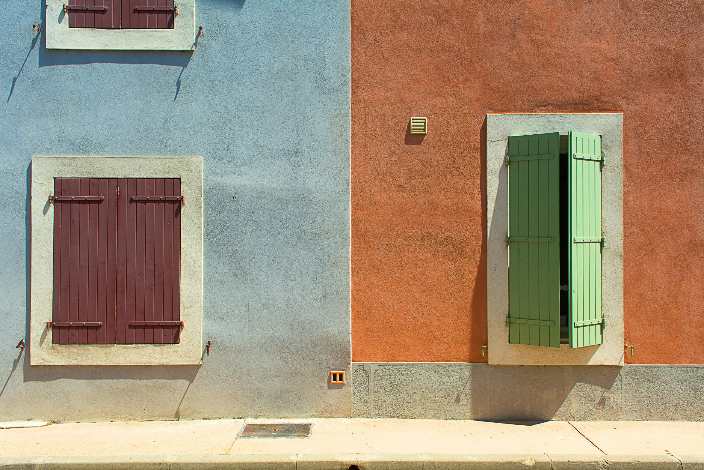 two windows and shutters painted orange, pink and green