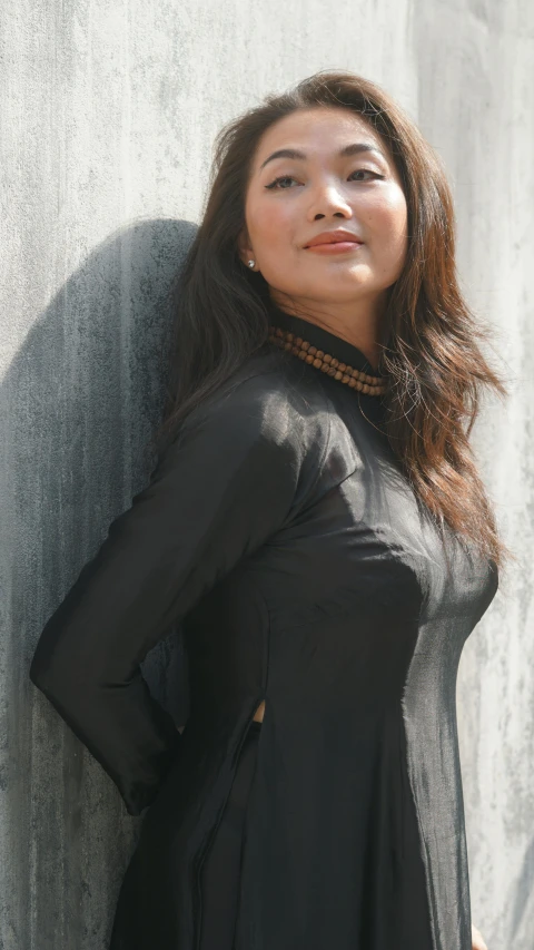 a young woman standing in front of a wall and wearing a black top