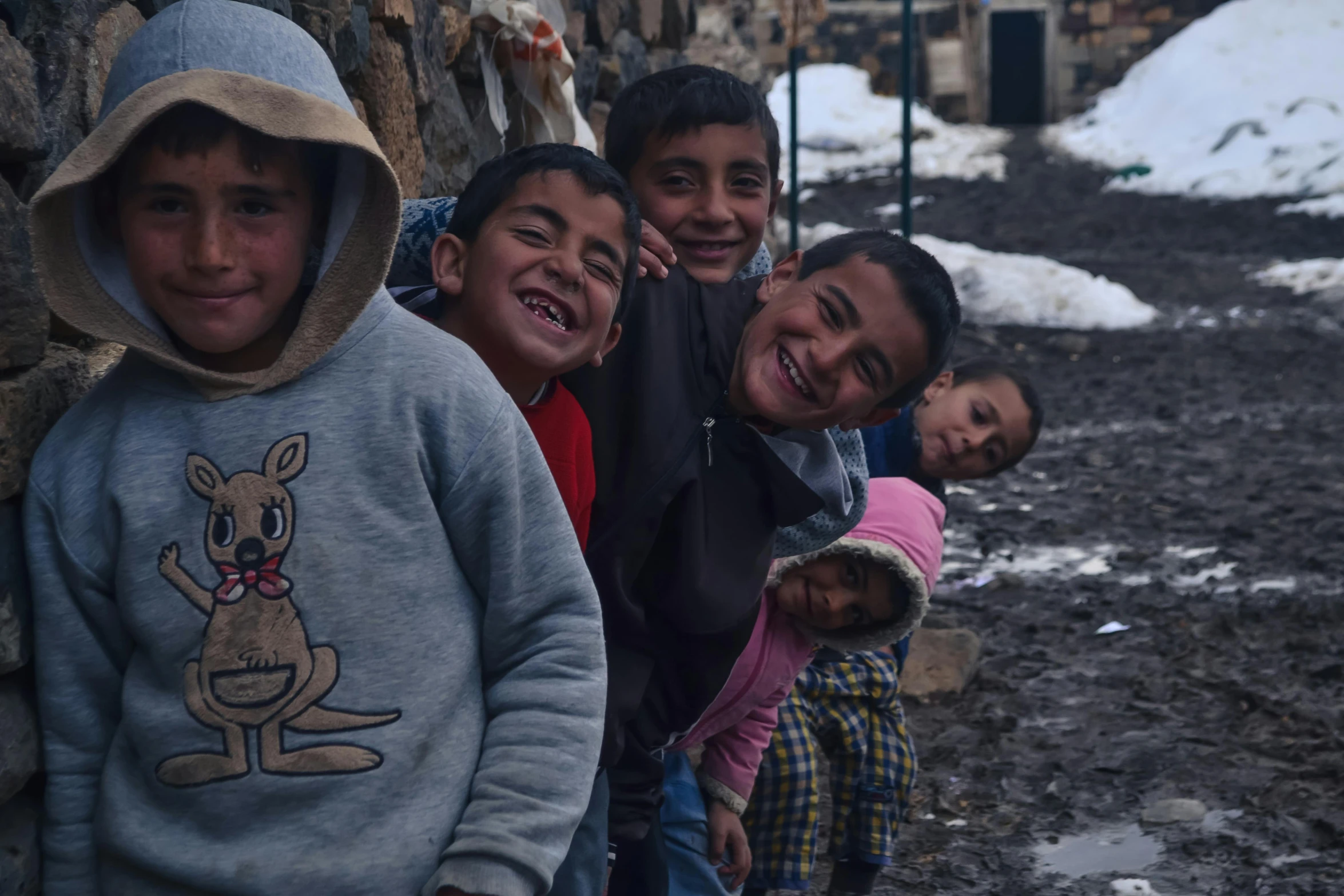 children standing in front of wall with snow on ground