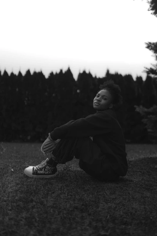 a person sits on the grass near some pine trees